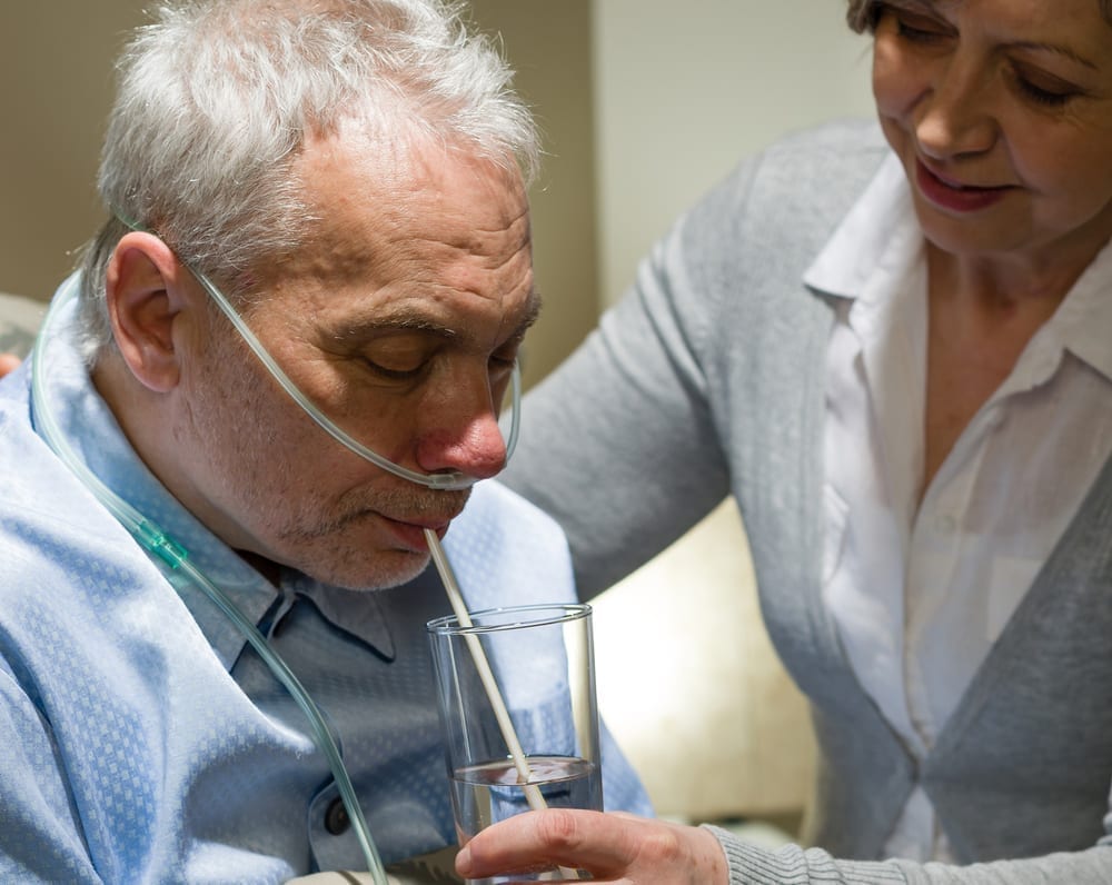 caregiver providing water for an elderly man who is wearing an oxygen tube