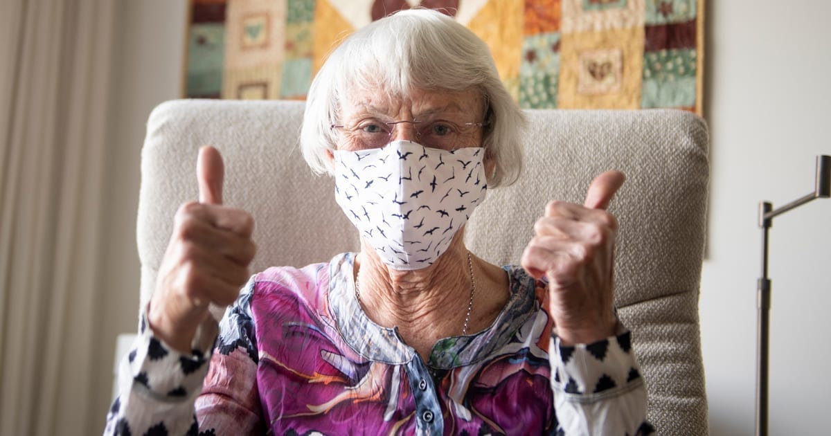 elderly woman in mask giving a thumbs up sign