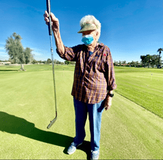 Woman wearing mask holding up a golf club on a golf course.
