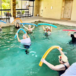 Experience the fun and invigorating exercise routine as residents raise pool noodles above their head in the pool at our vibrant assisted living community in Glencroft.